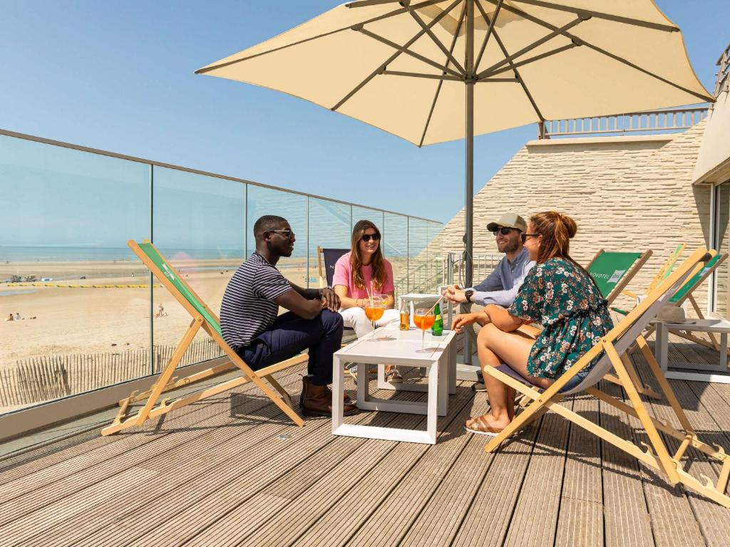 a group of people sitting at a table under an umbrella at ibis Thalassa Le Touquet in Le Touquet-Paris-Plage