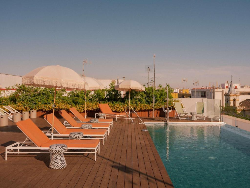 uma piscina com espreguiçadeiras e guarda-sóis num edifício em Ibis Styles Sevilla City Santa Justa em Sevilha