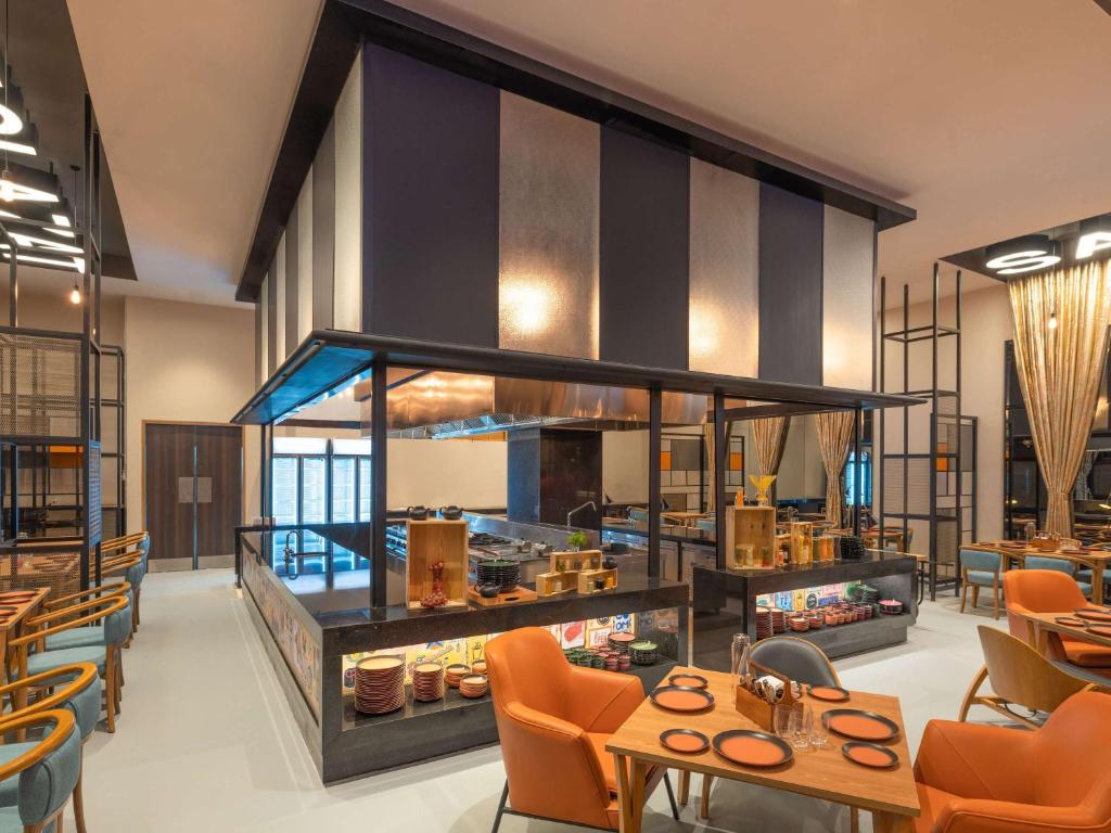 ibis Thane - An Accor Brand في ثين: مطعم فيه كراسي برتقالية وطاولات في الغرفة