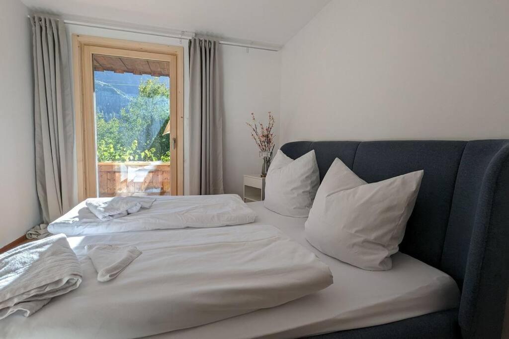 - un lit avec des draps et des oreillers blancs devant une fenêtre dans l'établissement großes Berg-Chalet in der Natur, à Bayrischzell