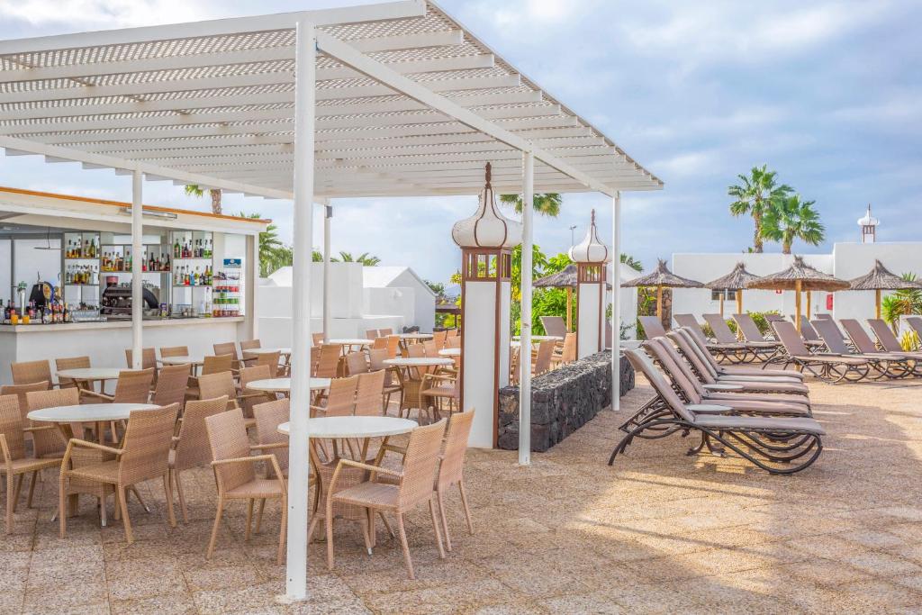 a patio with tables and chairs and a bar at Jardines del Sol in Playa Blanca