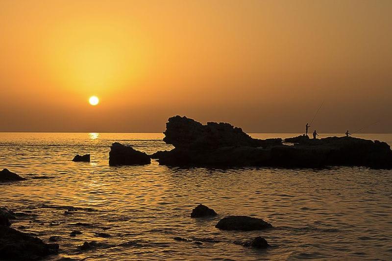 uma pessoa a pescar nas rochas no oceano ao pôr-do-sol em Suite Paradise - D111 em Caesarea