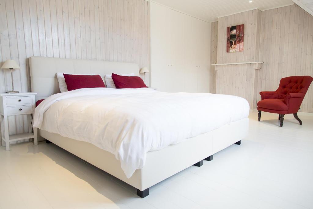 a white bedroom with a large bed and a red chair at Two White Pigeons in Ieper