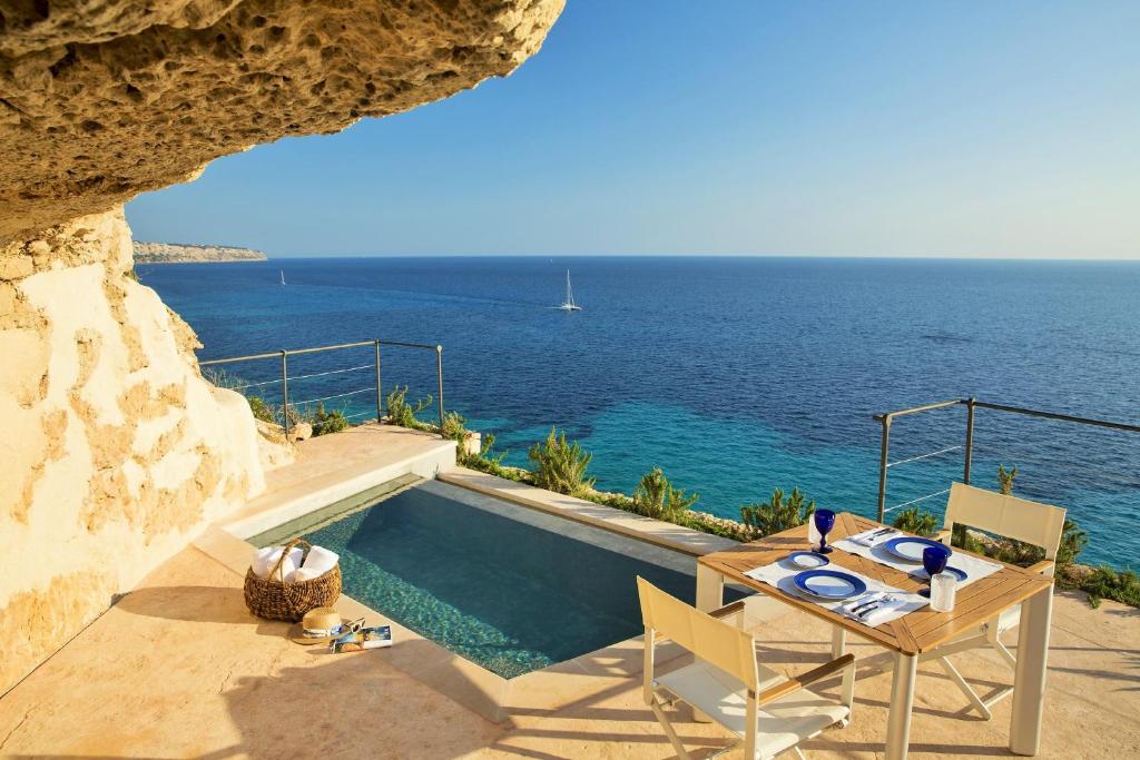 
a beach area with a pool, chairs, and a balcony at Cap Rocat, a Small Luxury Hotel of the World in Cala Blava
