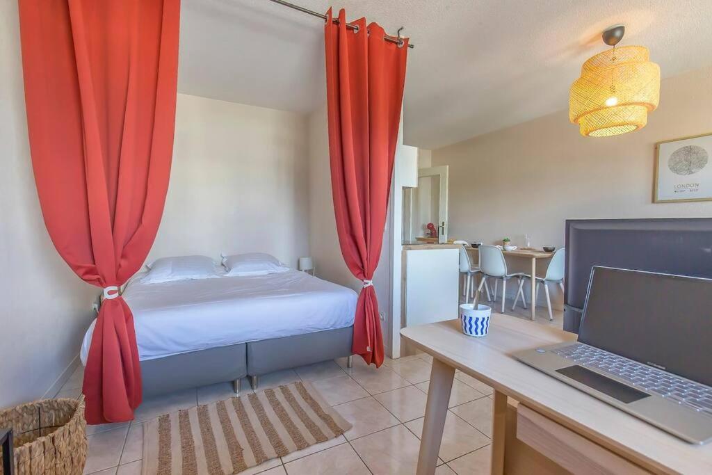 a bedroom with a bed with red curtains and a laptop at Maupassant: T1bis lit 160 - clim - parking gratuit in Grenoble