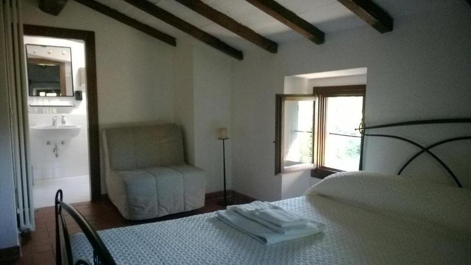 a white bedroom with a bed and a chair at Locanda dei Fienili del Campiaro in Grizzana