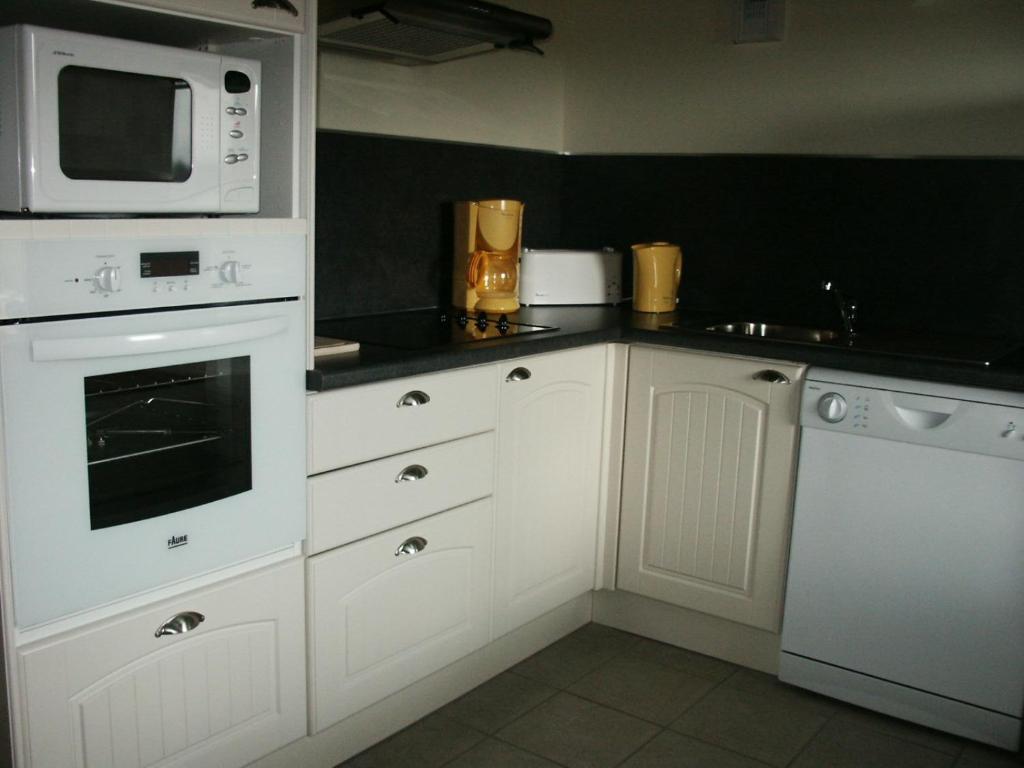 a kitchen with white cabinets and a microwave at Les Gîtes du Clos in La Tour-dʼAuvergne