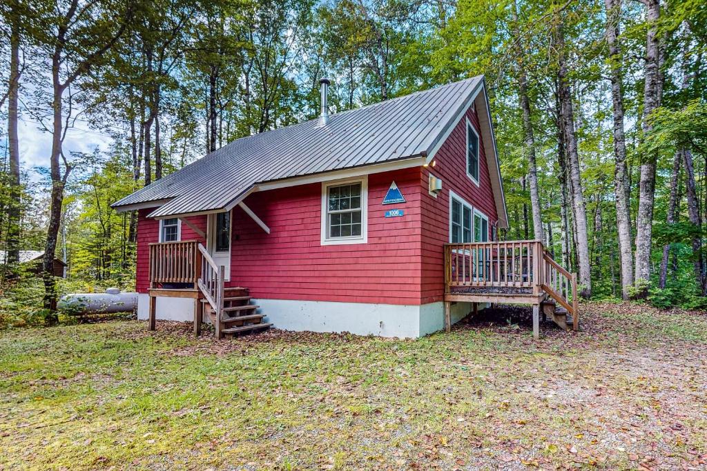 a small red house with a deck in the woods at Poplar Stream Chalet in Carrabassett