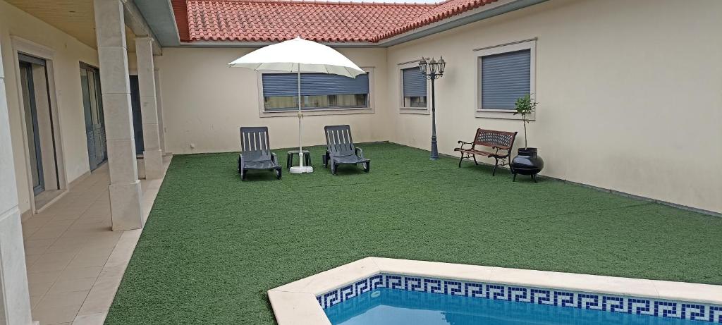 a backyard with a swimming pool and chairs and an umbrella at Vale Poços House in Vinha da Rainha