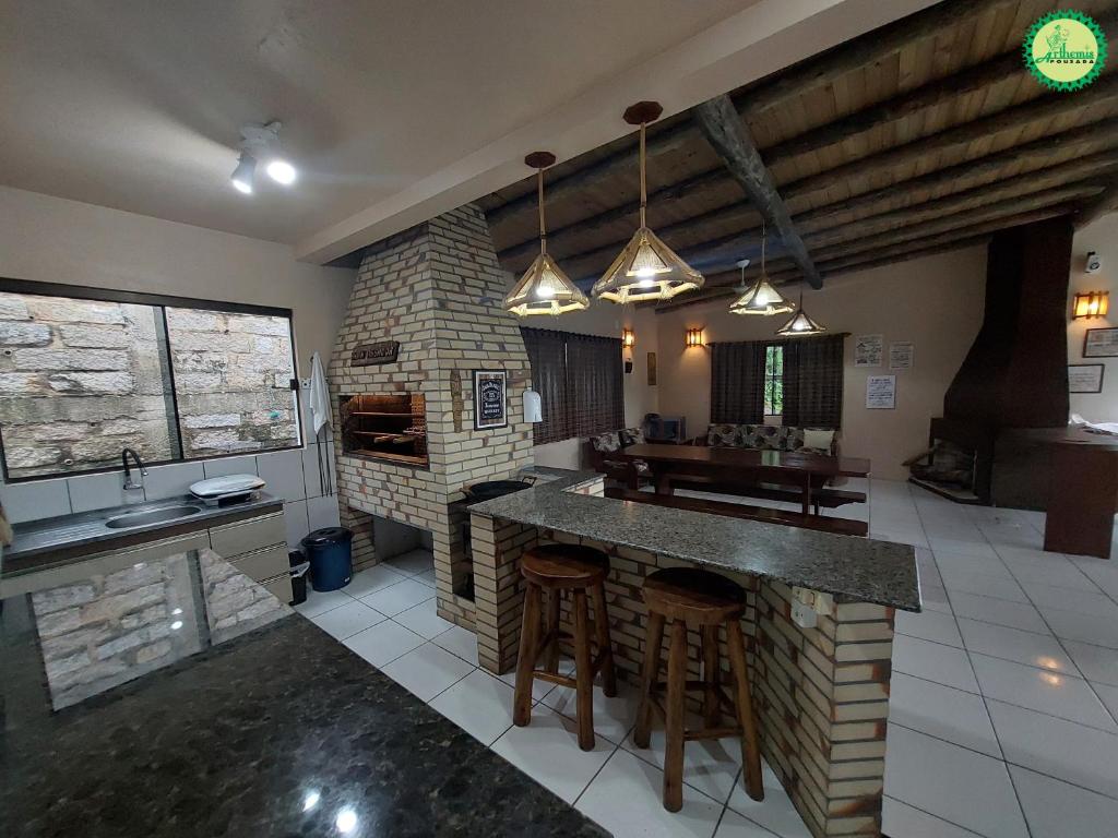 a kitchen with a stone fireplace and a kitchen with bar stools at Pousada Arthemis in Garopaba