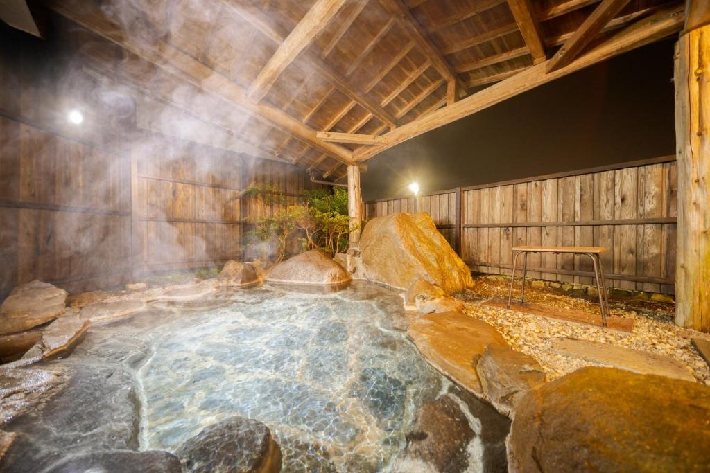 bañera de hidromasaje en una habitación con rocas y techo de madera en Osugi no Yado - Vacation STAY 43977v, en Yufu