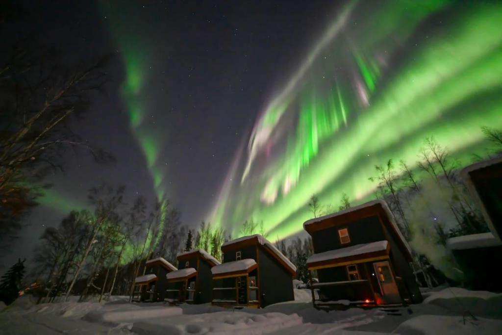 een rij hutten met het noorderlicht in de lucht bij The Lazy Lynx - Frontier Village in North Pole