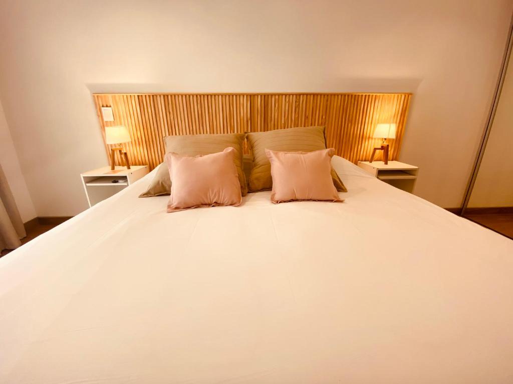 a large white bed with two pink pillows on it at Tigre Urban Suites in Tigre