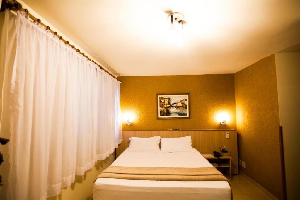 a bedroom with a large bed with white curtains at GOLDMEN HOTEL MARINGÁ in Maringá