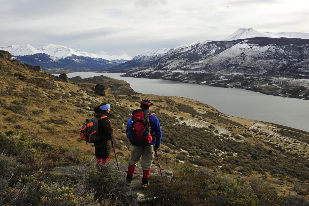 two people walking on a hill overlooking a lake at Remota Patagonia Lodge in Puerto Natales