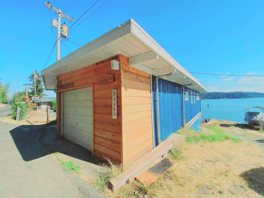 een klein houten gebouw met een garage naast het water bij The Coman's beach house in Hoodsport