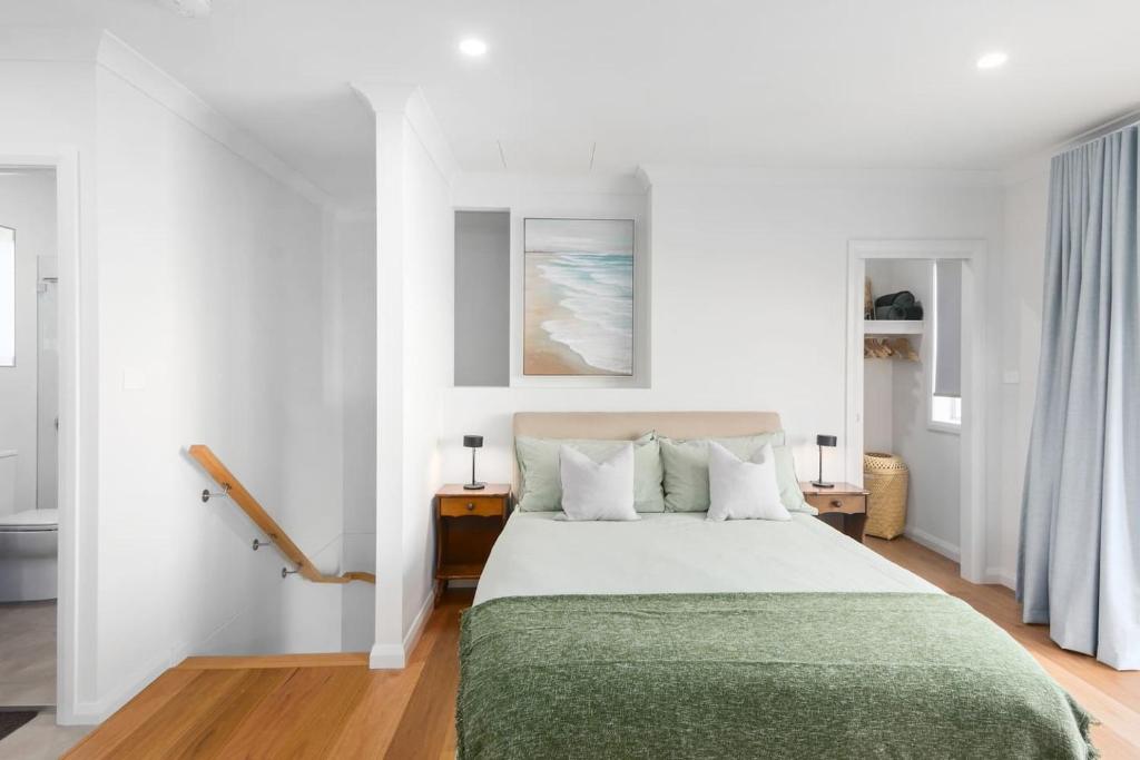 een witte slaapkamer met een bed met een groene deken bij Rockpool Escape - A Coastal Refresh with Balcony in Shellharbour