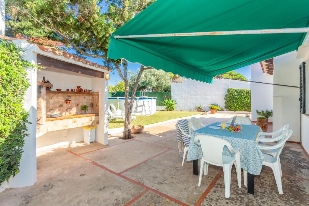 a patio with a table and chairs and a green umbrella at Sa Sivina in Cala en Bosc