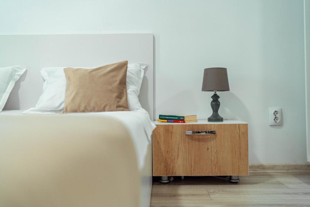 a bed with white sheets and a night stand with a lamp at Tatarasi Apartments - One Residence Iasi in Iaşi