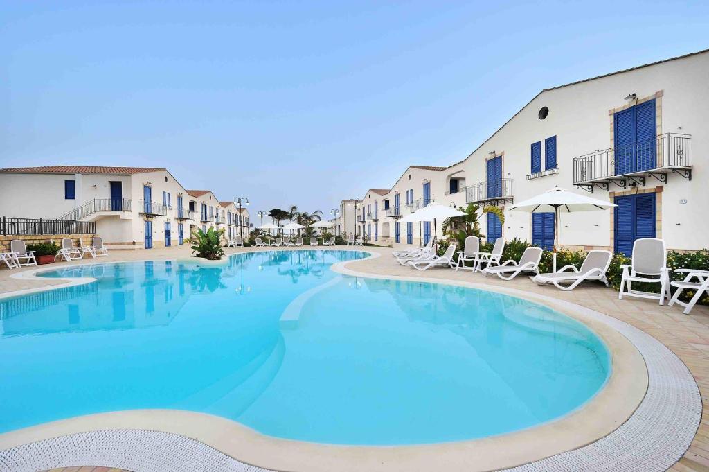 a large swimming pool with chairs and buildings at Scala Dei Turchi Resort in Realmonte