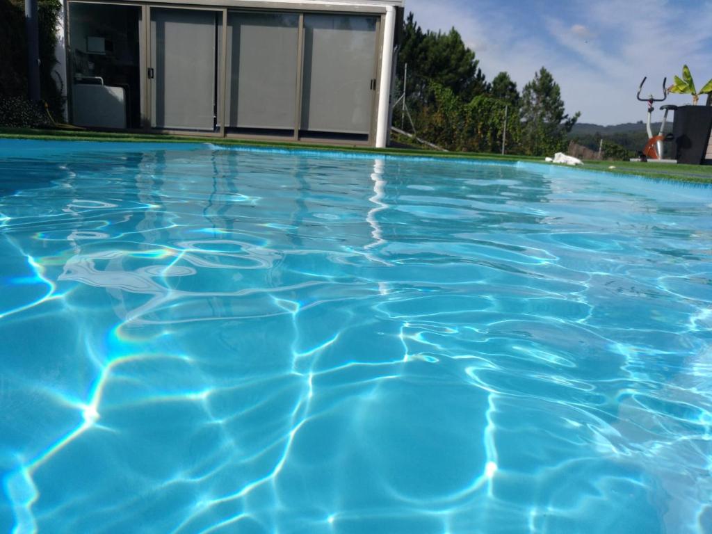 a swimming pool with blue water in front of a house at Casa Rocha Velha con piscina y terraza particular in Santiago de Compostela