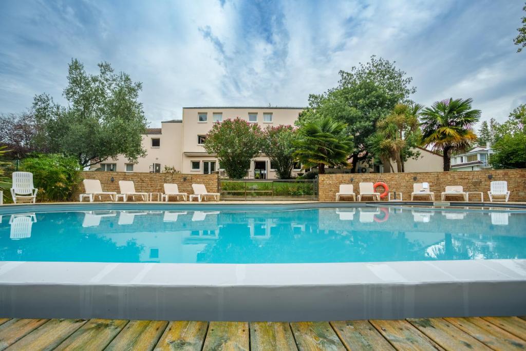 une piscine avec des chaises et un bâtiment en arrière-plan dans l'établissement Kyriad Nantes Sud - Bouaye Aéroport, à Bouaye