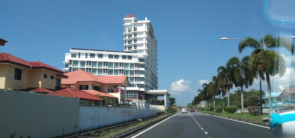 a city street with a tall white building and palm trees at PINTARMAN SERVICE APRTMENT @ THE STIRLING SUITES in Miri