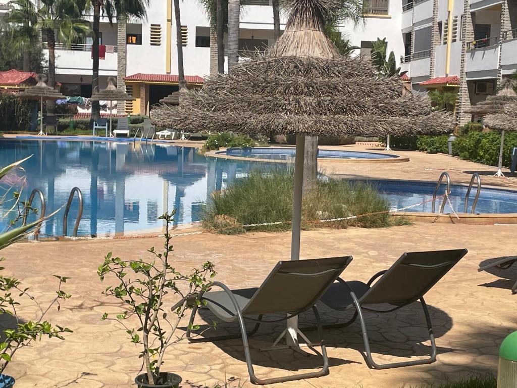 Bel appartement à skhirat plage et à 20 mn de Rabat في الصخيرات‎: كرسيين ومظلة أمام المسبح