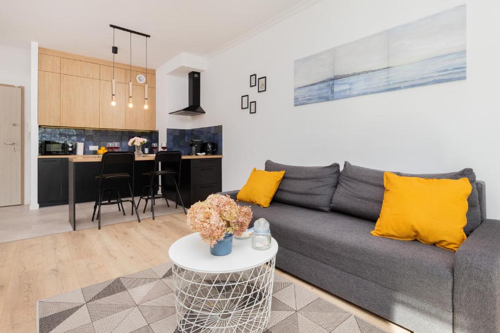 a living room and kitchen with a gray couch and yellow pillows at Modern Apartment with Balcony by Renters in Gdańsk