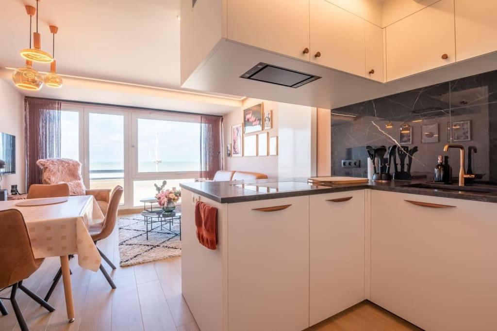 a kitchen with white cabinets and a dining room with a table at Appartement met frontaal zeezicht in Koksijde