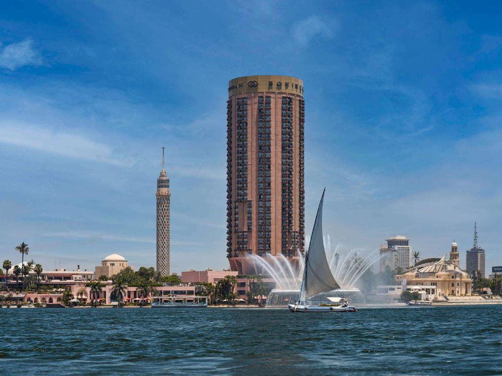 a sailboat in the water in front of a tall building at Sofitel Cairo Nile El Gezirah in Cairo