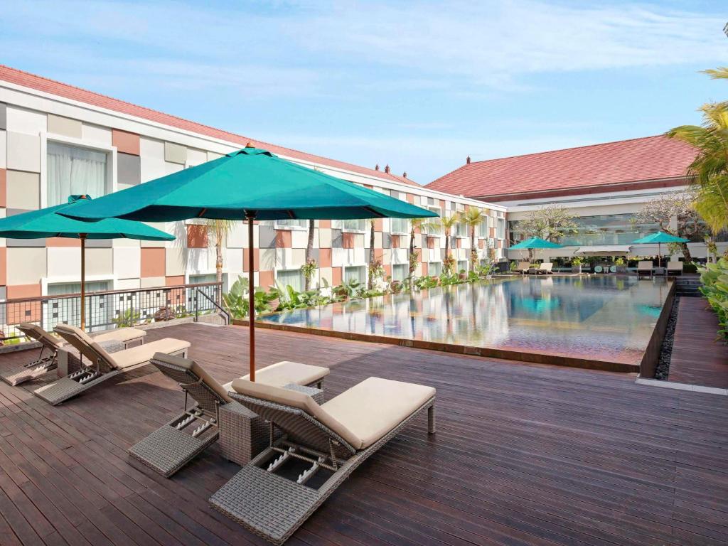 hotel z basenem, krzesłami i parasolem w obiekcie Novotel Bali Ngurah Rai Airport w mieście Kuta