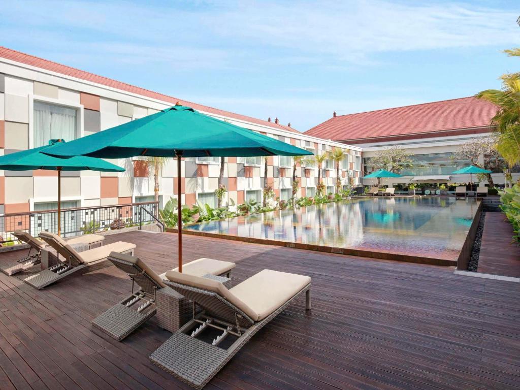 un hotel con piscina, sillas y sombrilla en Novotel Bali Ngurah Rai Airport, en Kuta