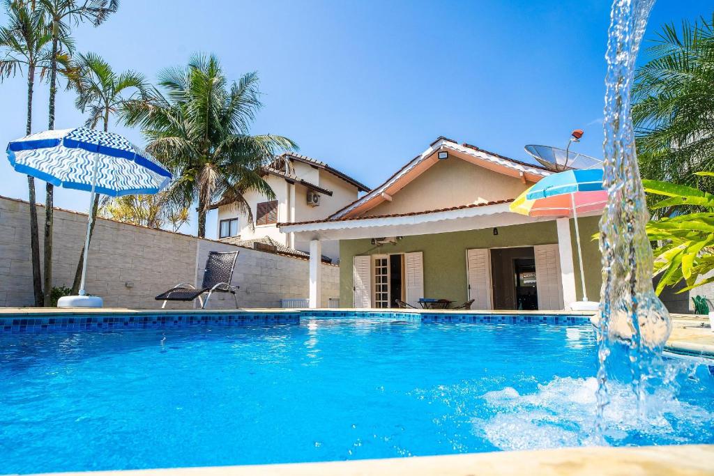 a swimming pool with an umbrella and a house at Maravilhosa casa no Cond. fechado Morada da Praia in Boracéia