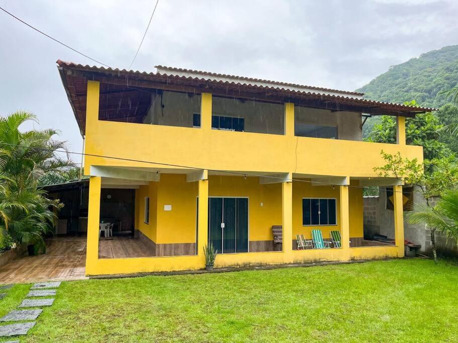 una casa amarilla con césped delante en Casa com churrasqueira e piscina, perto de riacho en Angra dos Reis