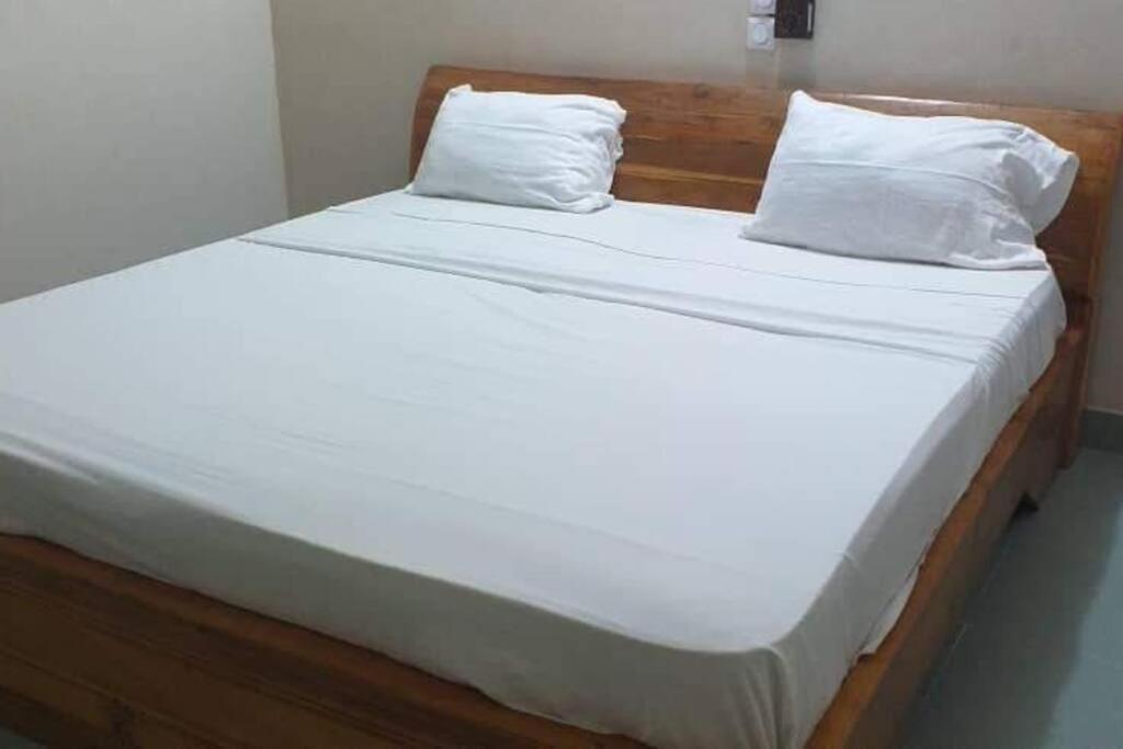 a bed with white sheets and two pillows at Ouidah Lodge in Ouidah