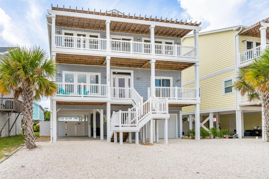a large house with white balconies and palm trees at Glimmering Shell Hideaway in Holden Beach