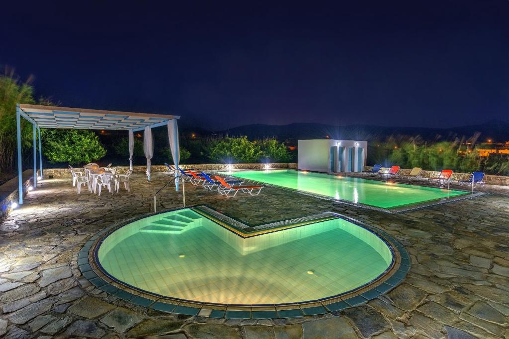 Hotel Smaragdi Apartments في فينيكاس: مسبح في الليل مع طاولة وكراسي