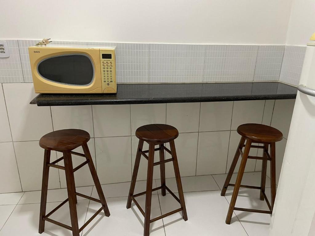 a microwave sitting on top of a counter with two stools at Pousada hostel praia itapua in Salvador