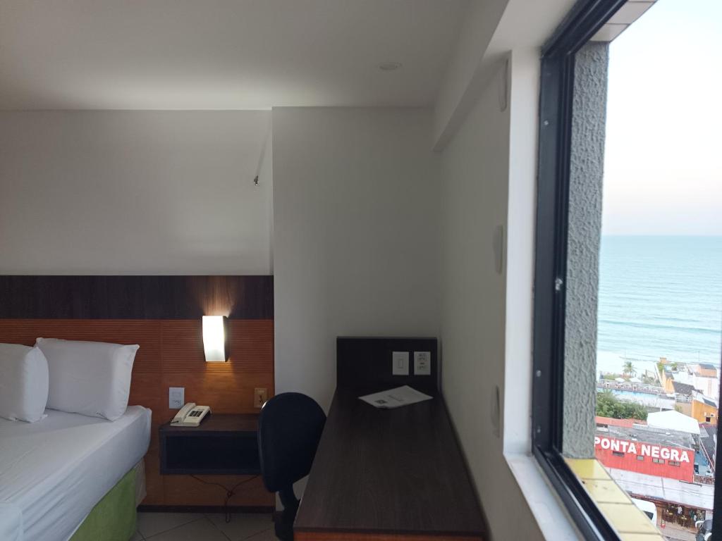 a room with a bed and a desk and a window at Natal Plaza requinte, conforto e vista para o mar in Natal