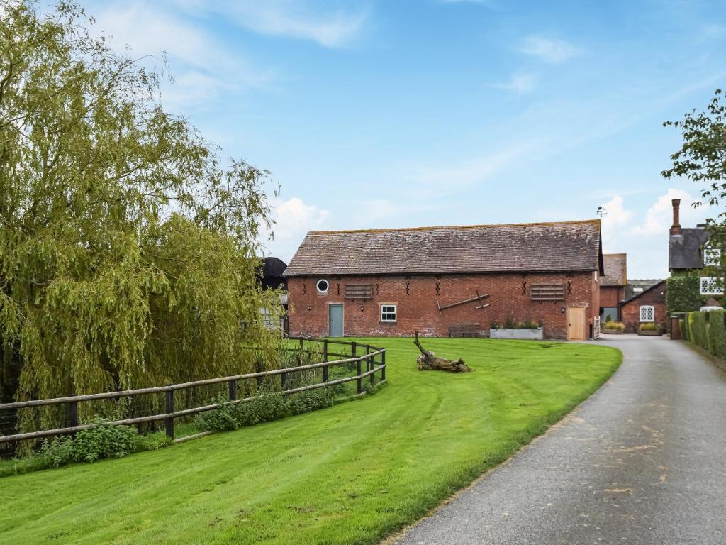 a farm house with a green lawn next to a road at The Barn in Nantwich