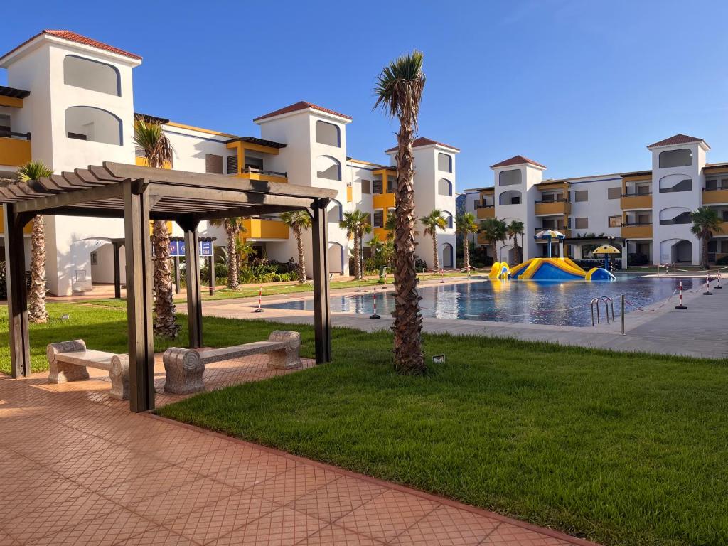 a park with a bench next to a swimming pool at Luxueux appartement avec piscine à la Marina Saidia in Saïdia