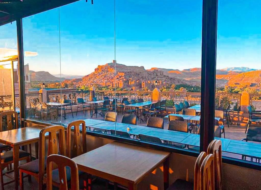 ein Restaurant mit Tischen und Stühlen und Bergblick in der Unterkunft Hôtel LAKASBAH Ait Ben Haddou in Aït-Ben-Haddou