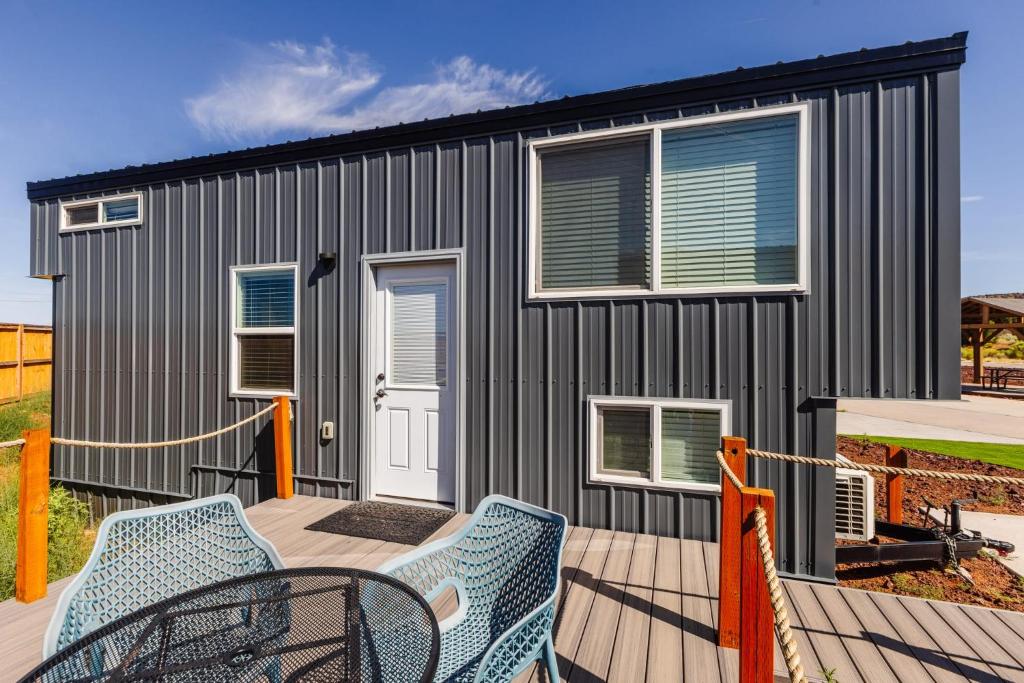 New calm & relaxing Tiny House w deck near ZION في Apple Valley: منزل صغير أسود مع شرفة وكراسي