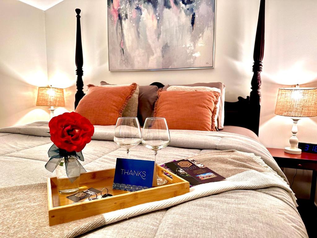 Bett mit einem Tablett mit Weingläsern und einer Rose in der Unterkunft Settlers Suites in Niagara on the Lake