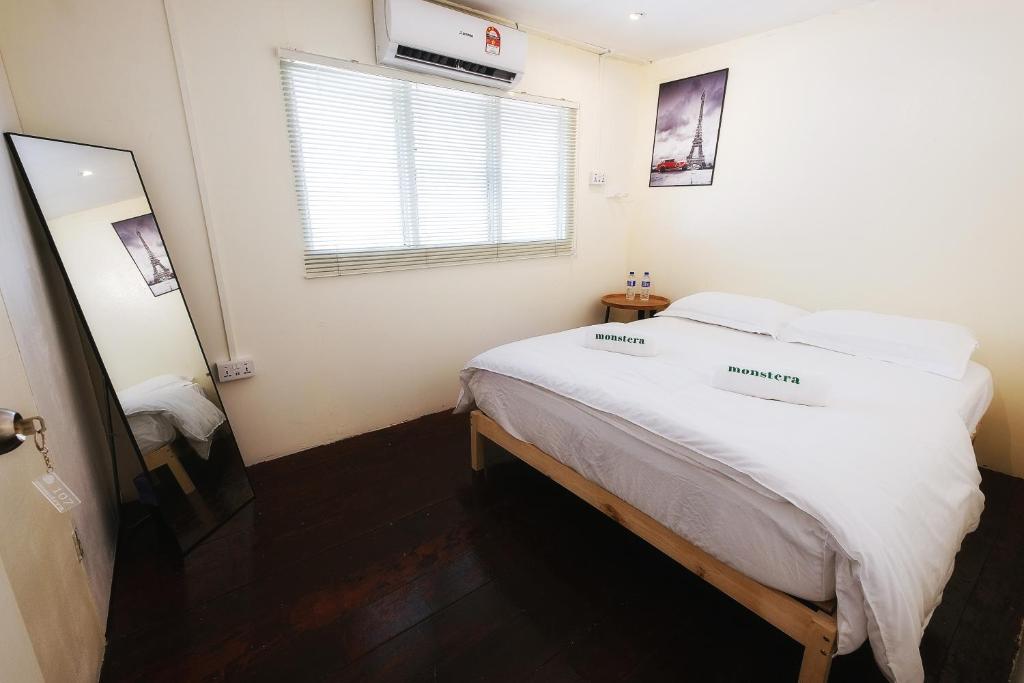 una camera da letto con un letto con lenzuola bianche e una finestra di monstera guesthouse (Lenggong) a Kampong Ulu Jepai