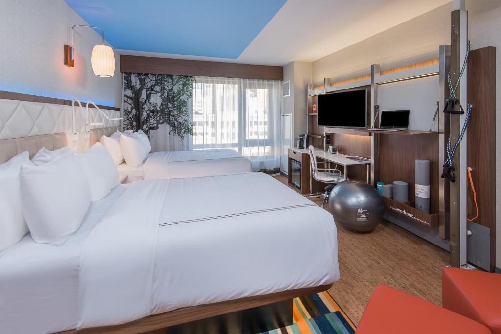 a bedroom with two beds and a desk and a television at EVEN Hotel New York - Times Square South, an IHG Hotel in New York