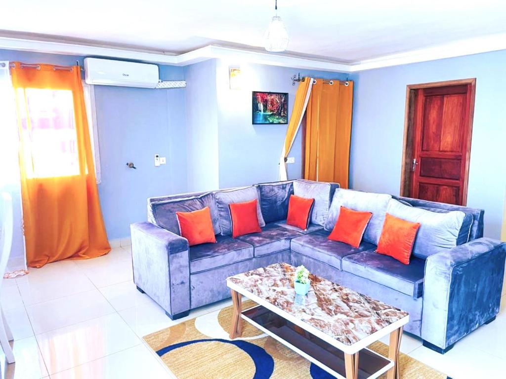 Sala de estar azul con sofá azul y almohadas de color naranja en Makeena Berry Cosy Mboa --, en Douala