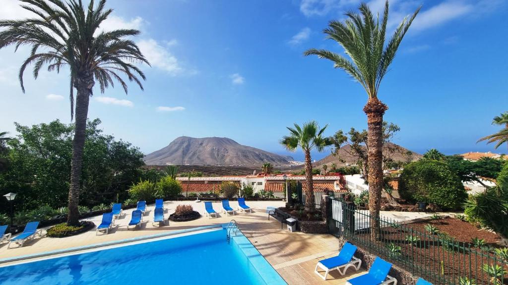 a pool with palm trees and a mountain in the background at Villa Azure Horizon and Breeze - Panoramic Ocean View and Heated Pool in Chayofa