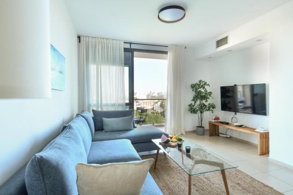 uma sala de estar com um sofá azul e uma televisão em Vibrant 2BR apt w Balcony 5-min from the Beach by Sea N' Rent em Tel Aviv